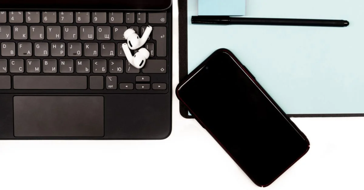 Gros plan d'un espace de travail avec un ordinateur portable, un smartphone et des écouteurs sans fil sur un bureau.