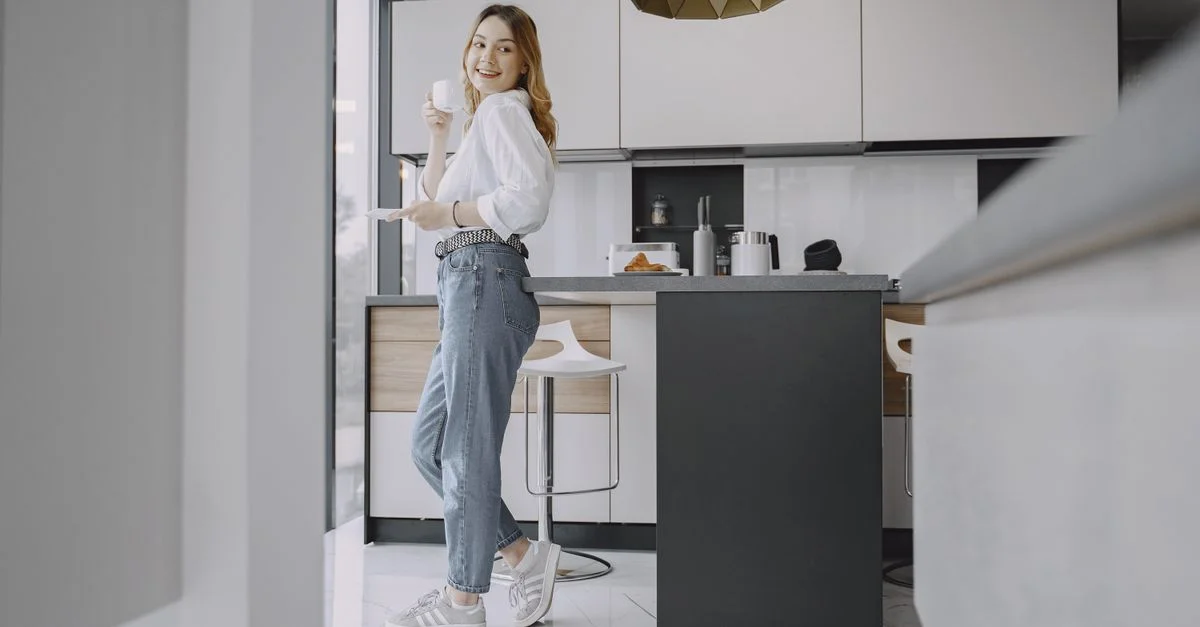 Femme en tenue décontractée appréciant une boisson chaude dans une cuisine moderne et stylée.