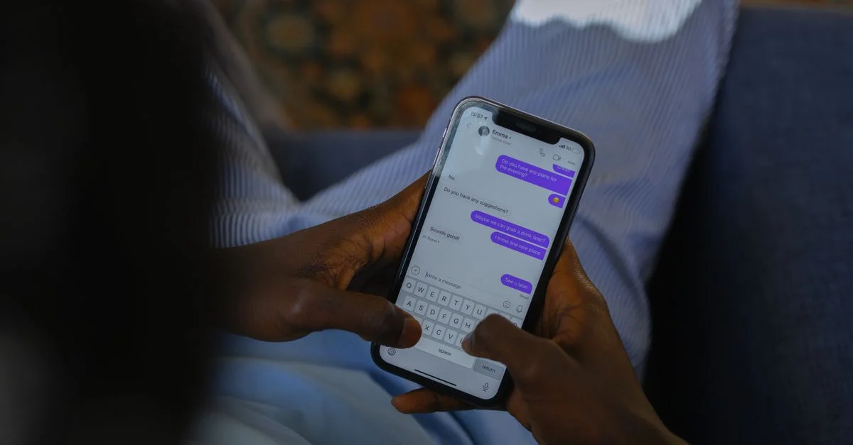 Gros plan de mains tenant un smartphone, tapant un message sur un écran tactile à l'intérieur.