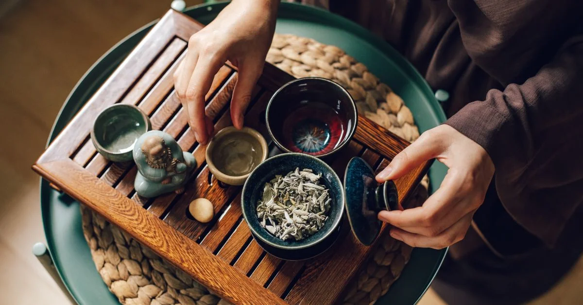 Vue aérienne d'une cérémonie du thé japonaise avec des tasses traditionnelles et des feuilles de thé sur un tapis tissé.