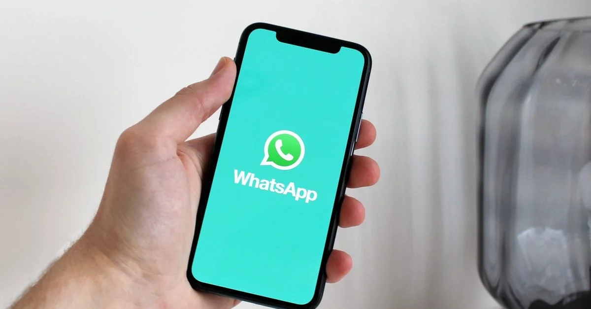 Gros plan sur une main tenant un smartphone affichant l'écran de l'application WhatsApp.
