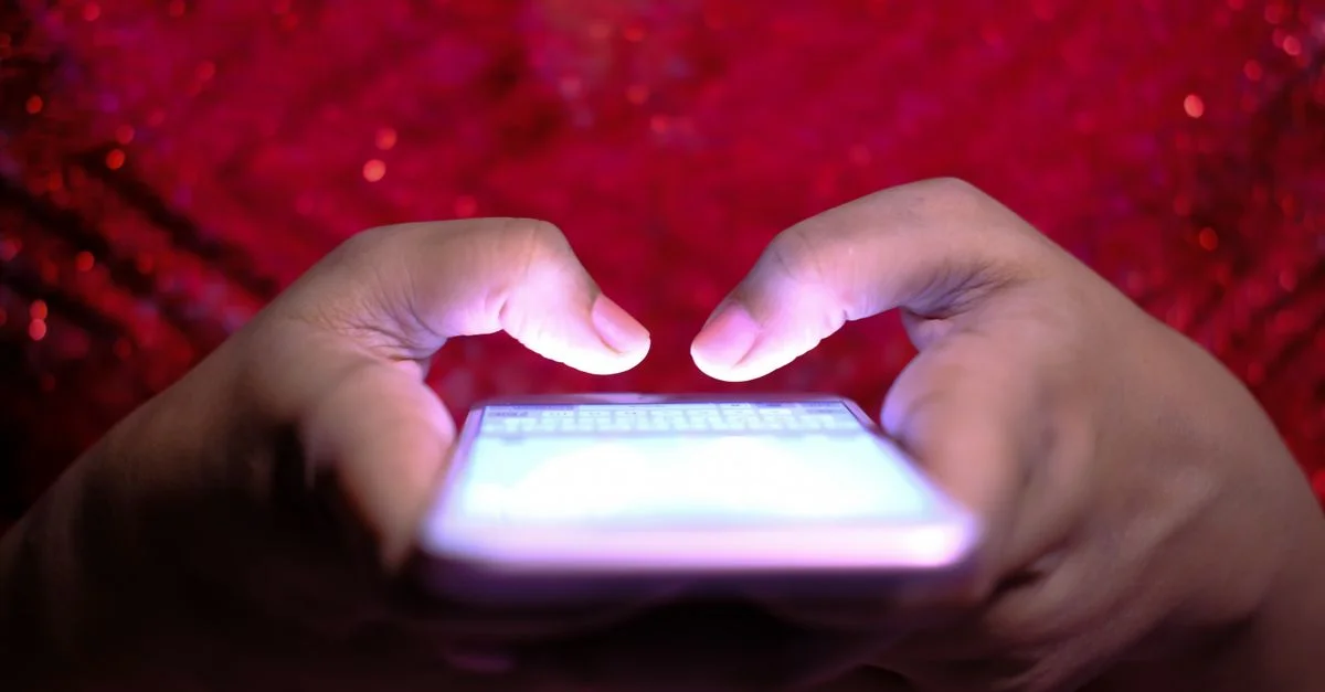 Mains tapant sur un smartphone avec un écran lumineux dans une faible luminosité, mettant en avant la technologie et la communication.